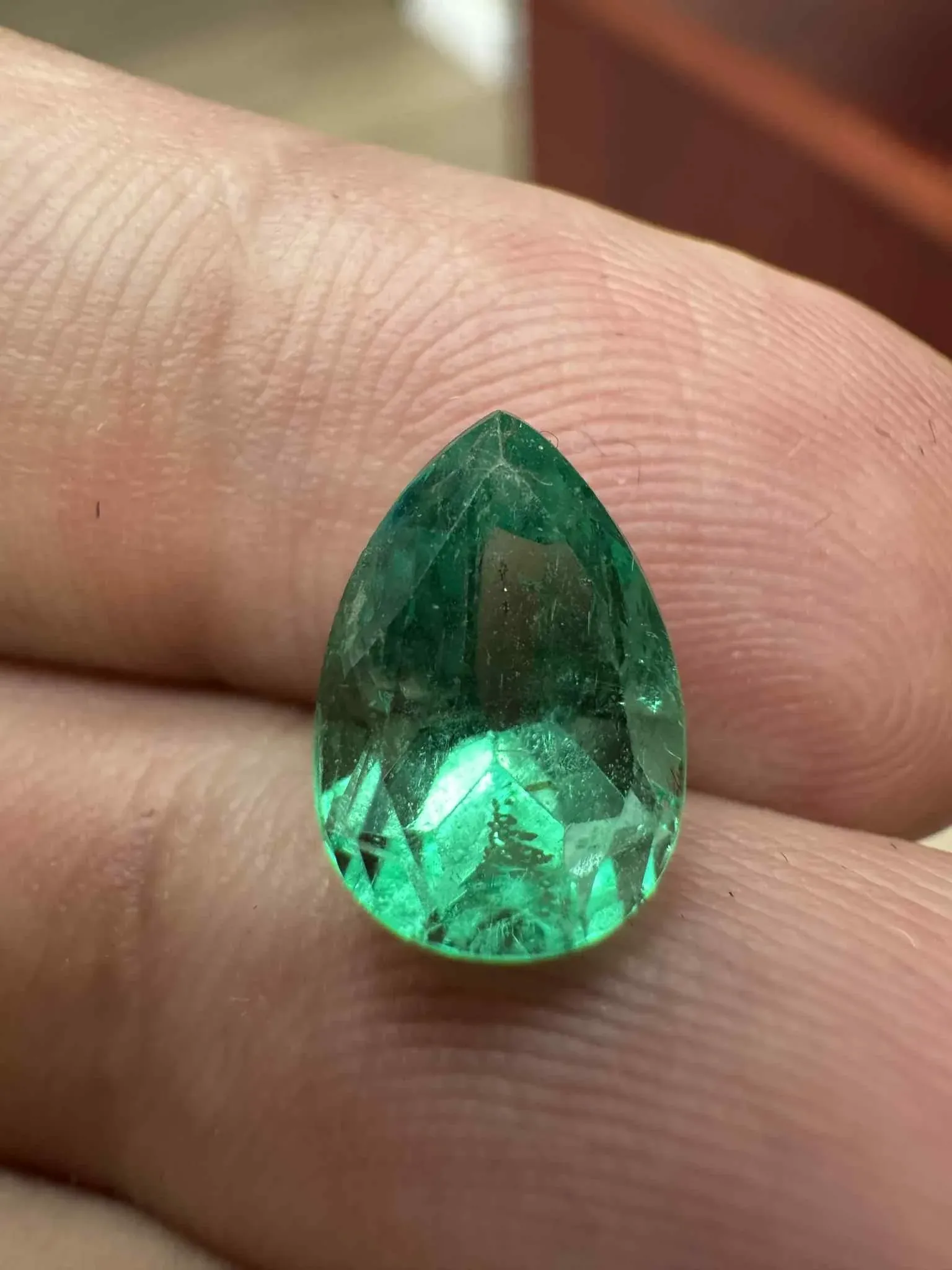 Colombian emerald gemstone held in hand showing deep green glow and natural jardine, sourced by A. D'Mae Diamonds Los Angeles